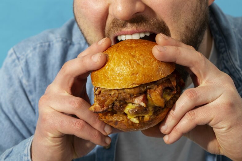 Tierische_Fette__1_.jpg Eine Person hält einen saftigen Burger mit einem goldenen Brötchen und beabsichtigt, ihn zu essen.