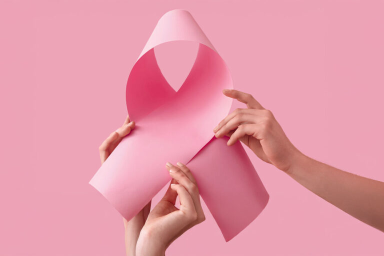 Zwei Hände halten ein rosa Papier, das zu einer Schleife geformt ist, vor einem pinken Hintergrund.