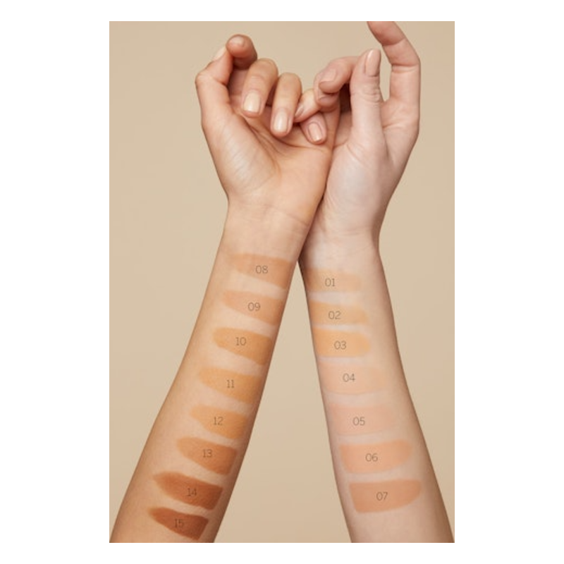 Zwei Hände mit Farbtests für Makeup-Töne auf den Unterarmen, nummeriert von 01 bis 15 auf einer neutralen Hintergrundfarbe.