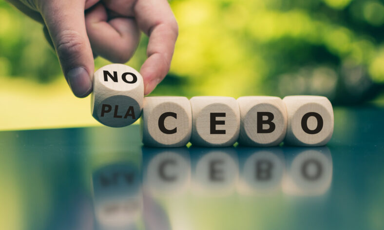 Holzwürfel mit Buchstaben, die das Wort 'NO PLACEBO' bilden, auf einem Tisch in der Natur.