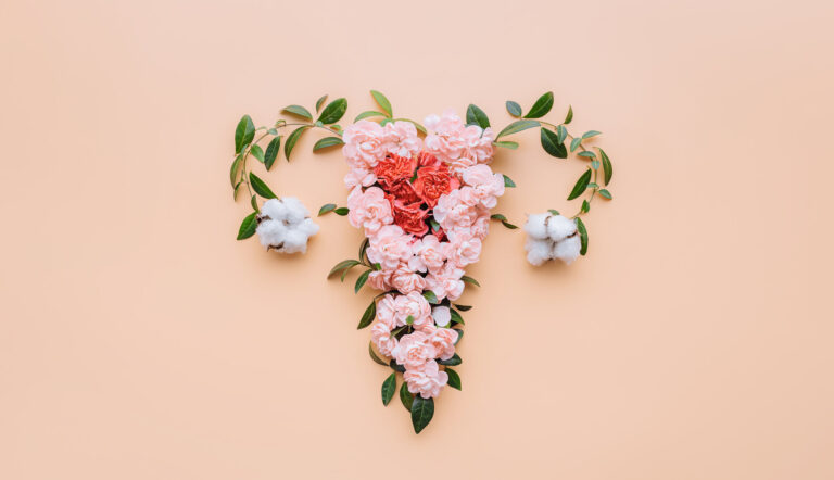 Ein florales Arrangement in Herzform aus rosa Blumen und Baumwollblüten auf einem pfirsichfarbenen Hintergrund.