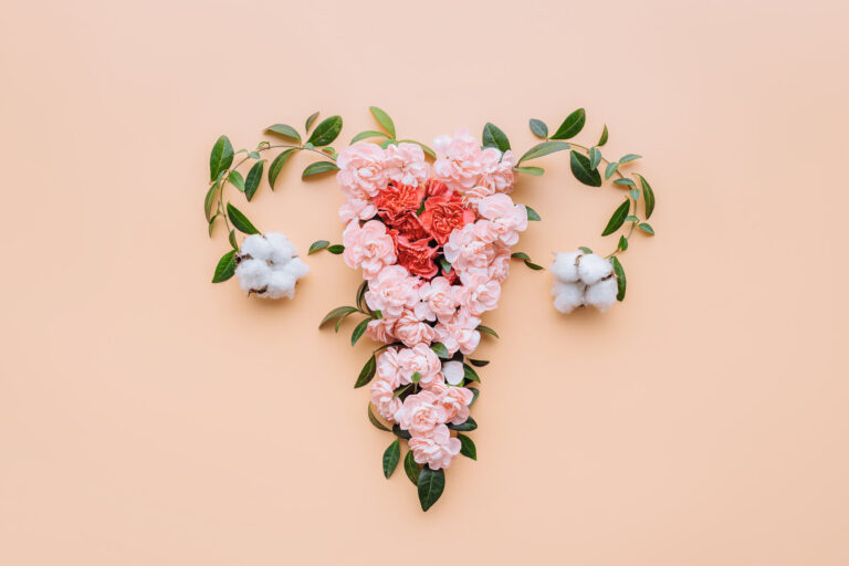 Ein florales Arrangement in Herzform aus rosa Blumen und Baumwollblüten auf einem pfirsichfarbenen Hintergrund.