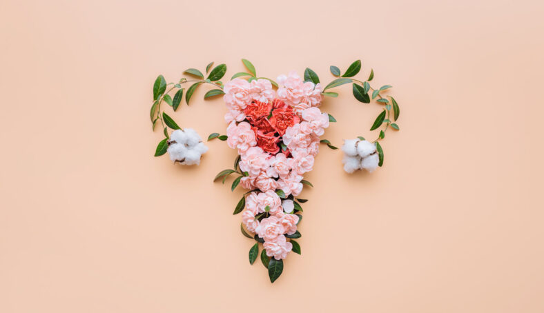 Ein florales Arrangement in Herzform aus rosa Blumen und Baumwollblüten auf einem pfirsichfarbenen Hintergrund.