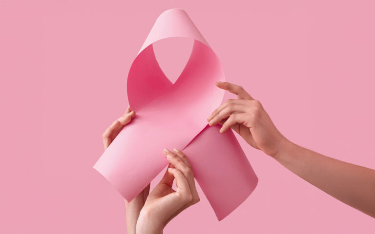Zwei Hände halten ein rosa Papier, das zu einer Schleife geformt ist, vor einem pinken Hintergrund.