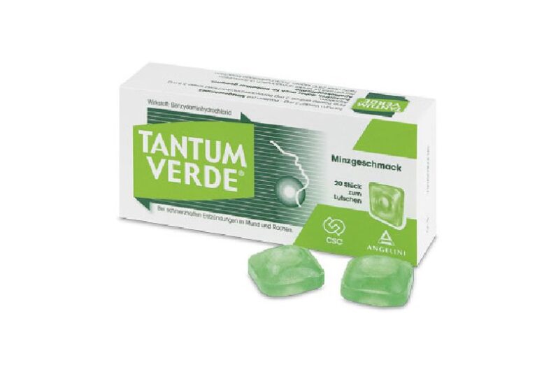 Packung mit Tantum Verde Lutschtabletten in Minzgeschmack, zwei Tabletten liegen daneben.